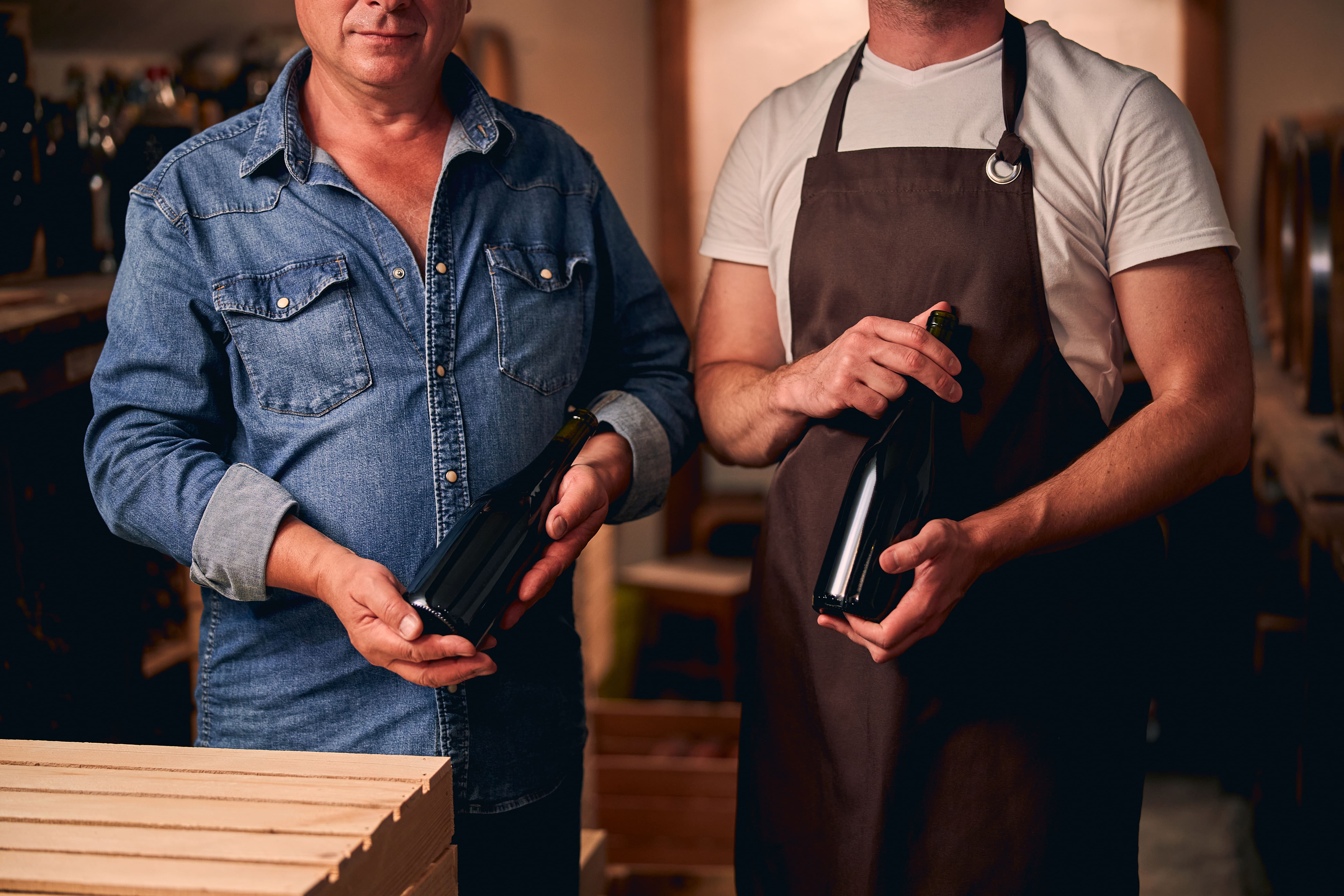 Two sommeliers holding red wine bottles.